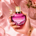 Close up of Aigner Starlight Gold Eau de Parfum elegant pink bottle featuring a gold cap and letter charm on a marble surface next to pink flowers at perfumesouq qatar