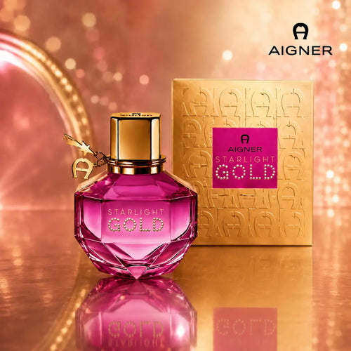 Aigner Starlight Gold Eau de Parfum pink crystal bottle standing next to its embossed gold packaging box against a shimmering gold bokeh background available at perfumesouq qatar